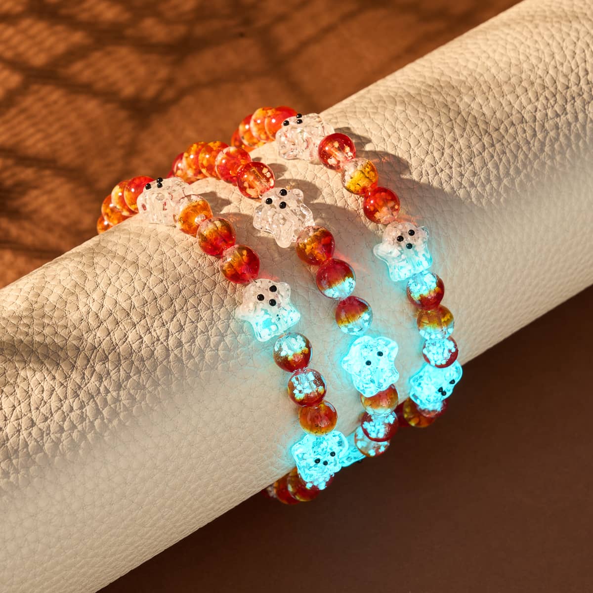 Berry Boo Silver Firefly Glass Ghost bracelets with glowing glass beads in orange and blue on textured beige display by NOGU